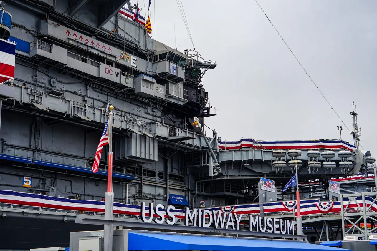 Et stort gråt skib med flag og skiltet USS Midway Museum ved indgangen.