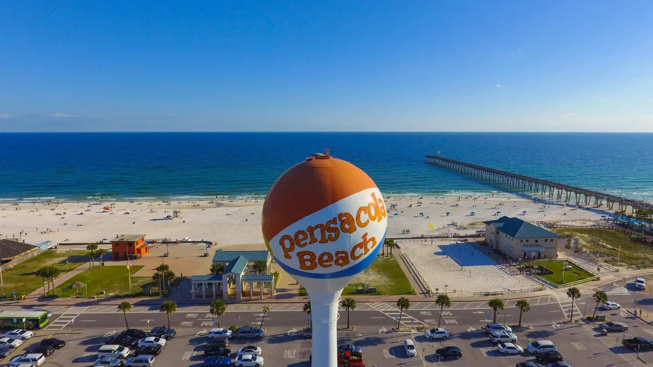 Vandtårnet med teksten Pensacola Beach foran en bred sandstrand og en lang mole.