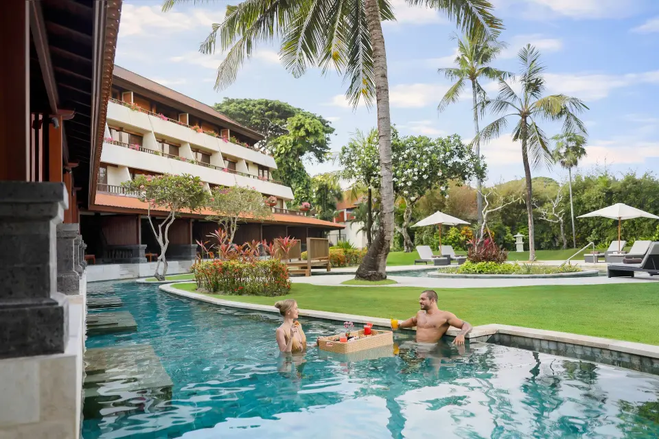 To gæster ved en flydende serveringsbakke i poolen foran hotellets have.