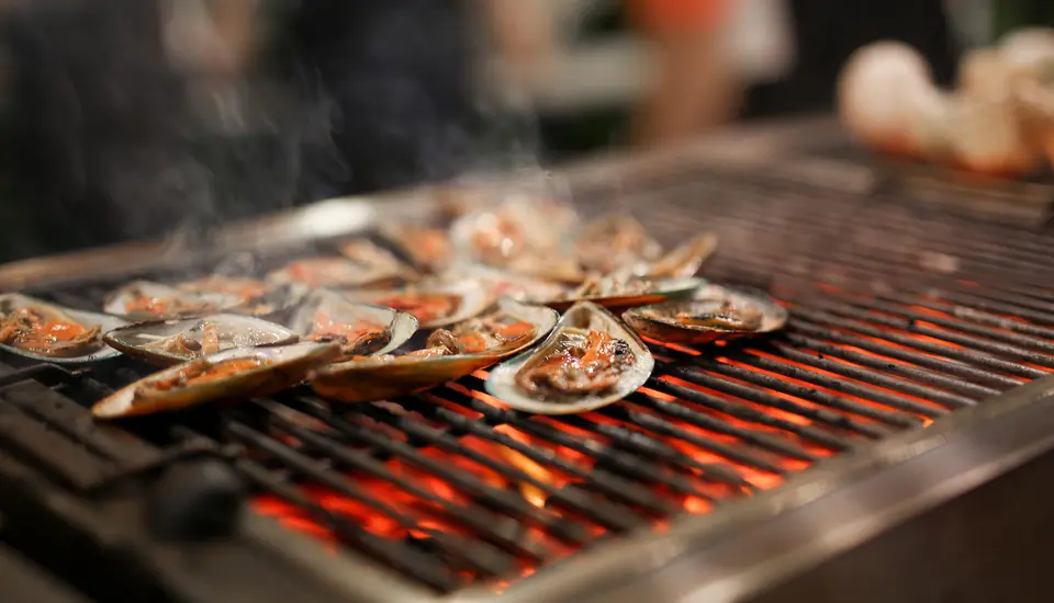 Åbne skaldyrsskaller på en varm grill med glødende kul.