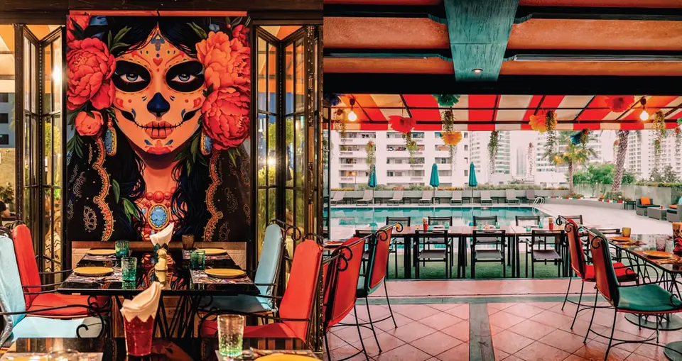 Restaurant ved poolen med farverige stole og et stort vægmaleri på Rembrandt Hotel Bangkok.