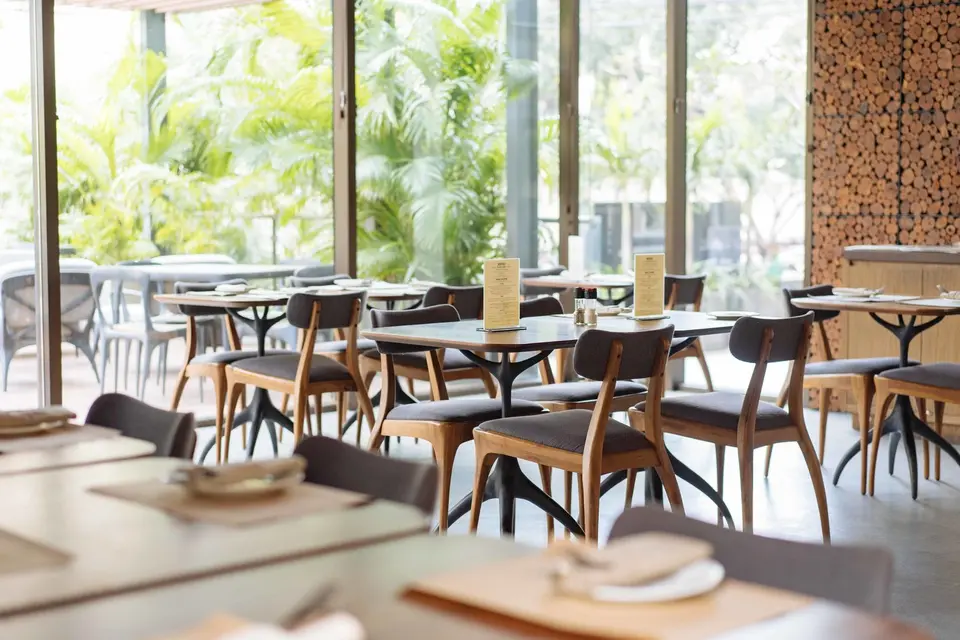 Restaurant med dækkede træborde og glaspartier ud mod grønne planter.