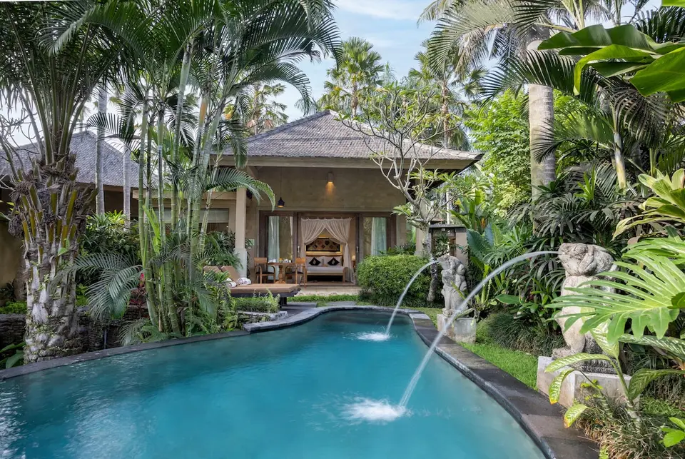 Pool med vandstråler og grøn beplantning foran en villa hos The Sankara Resort & Spa.