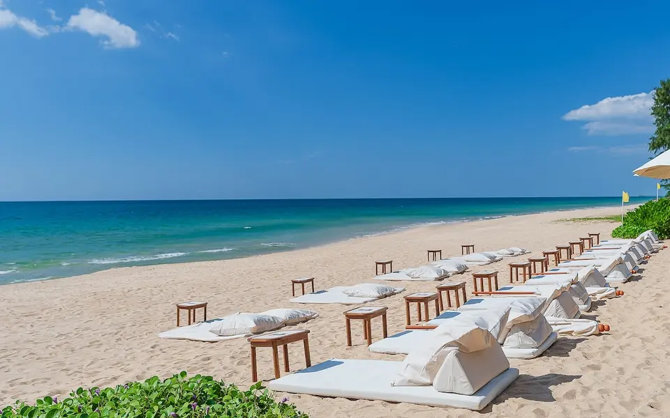 Santhiya Phuket Natai: Sandstrand med polstrede liggestole og små træborde ved havet.