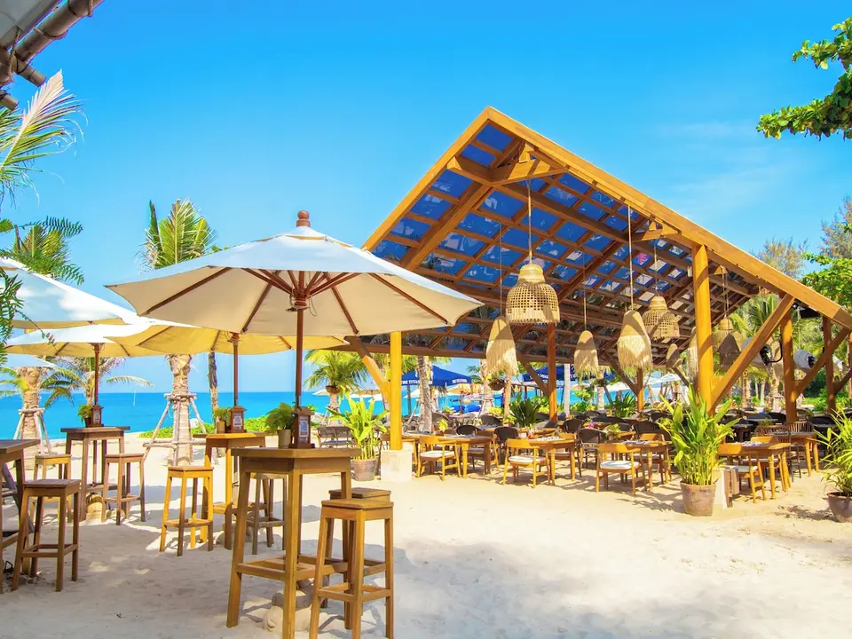 Santhiya Phuket Natai: Åben restaurant ved stranden med borde, stole og parasoller.