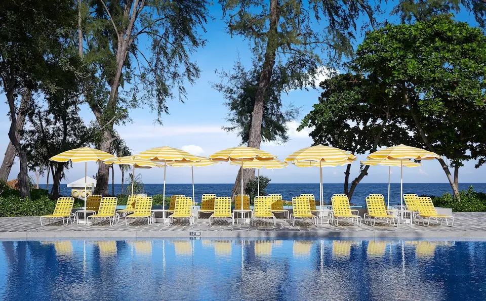 Pool med gule liggestole, stribede parasoller og havudsigt på The Standard Hua Hin.