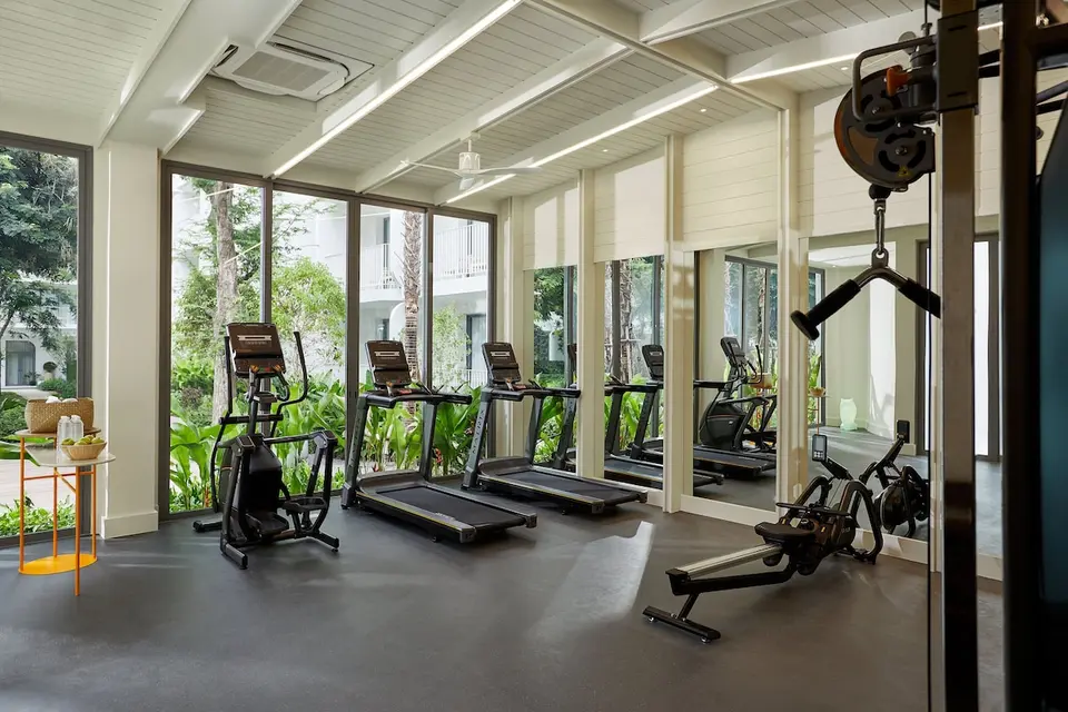 Fitnessrum med træningsmaskiner og store vinduer mod haven på The Standard Hua Hin.