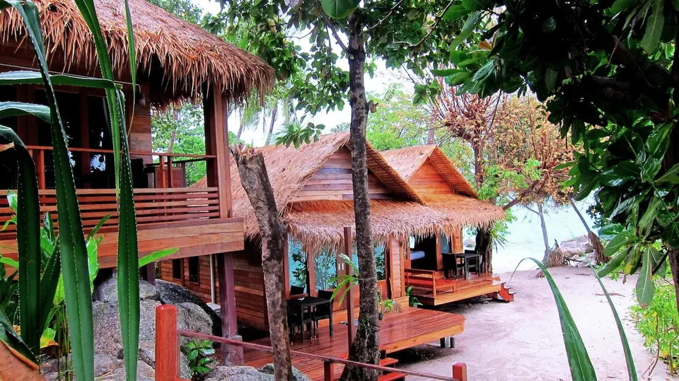 Bungalows med stråtag mellem træer ved stranden på Ten Moons Lipe Beach Resort.