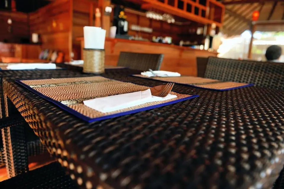 Dækket bord med flettede stole og bar i baggrunden på Ten Moons Lipe Beach Resort.