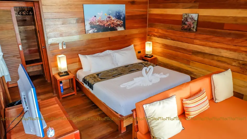 Værelse med dobbeltseng, sofa, tv og træbeklædte vægge på Ten Moons Lipe Beach Resort.