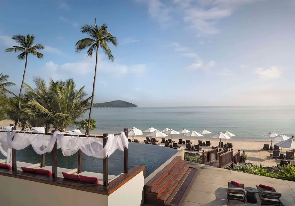 Pool med liggestole og parasoller med udsigt over stranden på Lawana Samui Resort