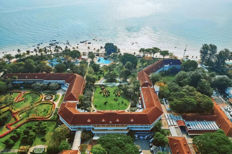 Luftfoto af hotellets røde tage, haver og pools ved stranden.