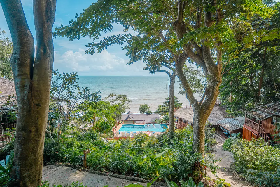 Udsigt mellem træerne til poolen, bungalows og havet på Koh Jum Resort.