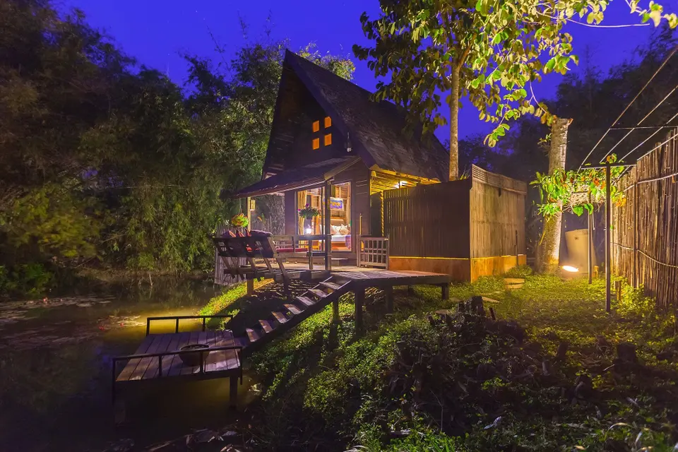 Træhus beliggende nær en rolig dam, oplyst om natten, Lanjia Lodge i Chang Rai