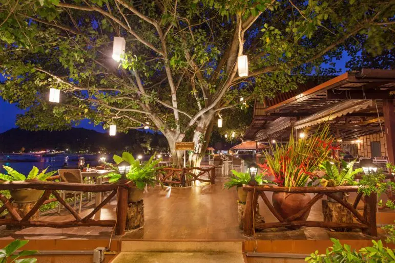 Restaurantterrasse med oplyst træ og borde ved havet på Phi Phi Natural Resort om aftenen.