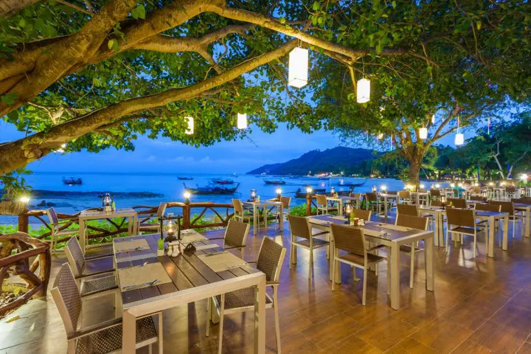 Restaurantborde under et træ med lanterner og havudsigt på Phi Phi Natural Resort ved skumring.