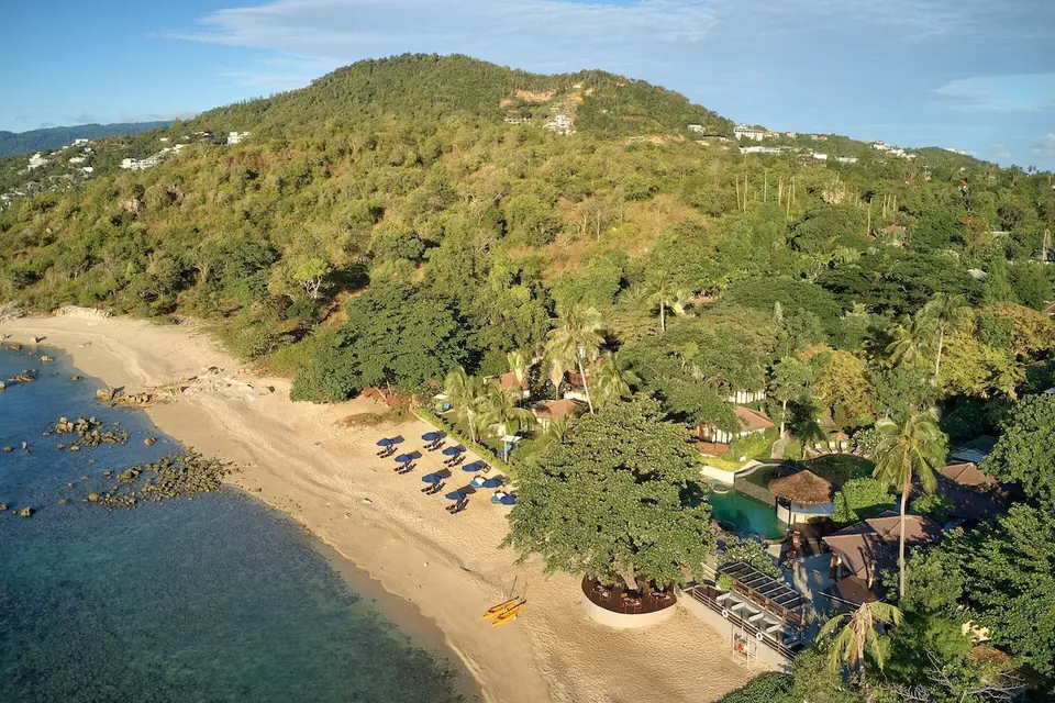 Luftfoto af resortets bygninger og strand langs en grøn skråning.