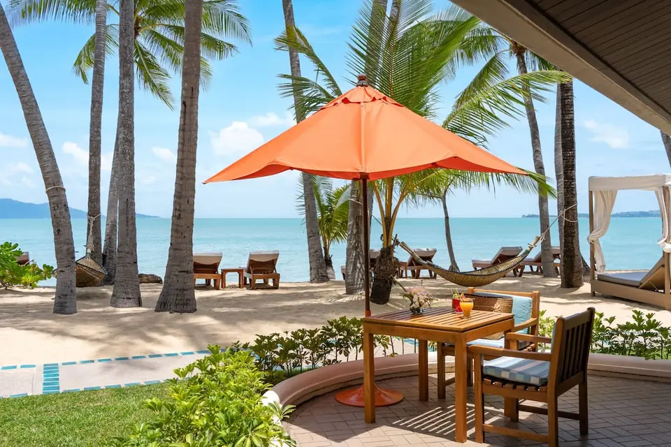 Terrasse med bord, stole og orange parasol ved stranden på Santiburi Koh Samui.