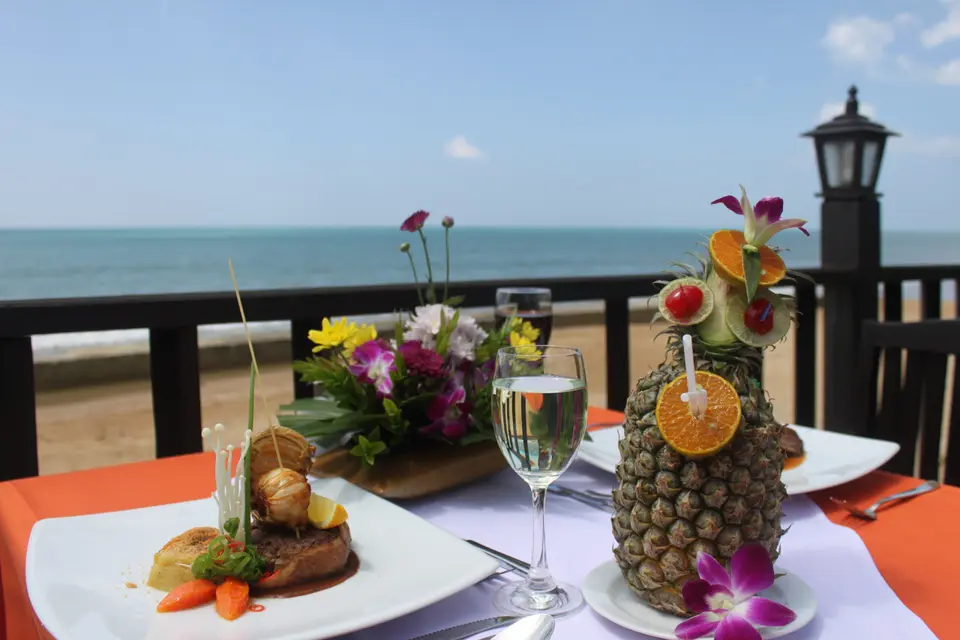 Dækket bord med mad, en drink i en ananas og udsigt over havet ved Sudala Beach Resort.