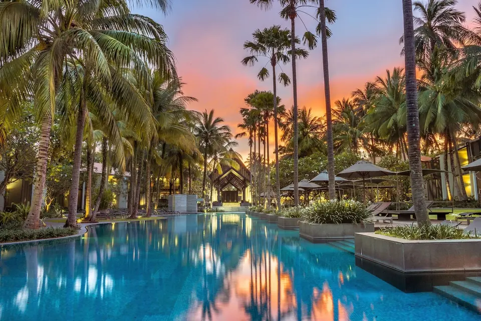 Pool omgivet af palmer og liggestole i skumringen på Twinpalms Phuket