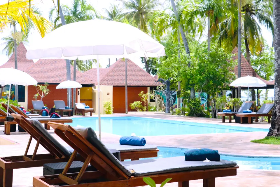 Afslappende stemning ved poolen på Sivalai Beach Resort med palmer, hvide parasoller og hyggelige bungalows i solen.