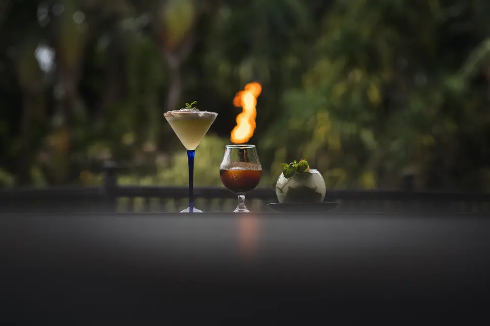 Tre cocktails på et bord med en flamme og grønne planter i baggrunden.