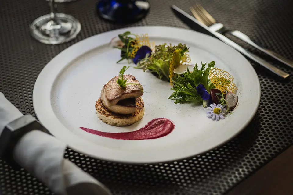 Elegant gourmetmiddag serveret med blomster og grønt på hvid tallerken, klar til nydelse i hyggelig restaurantstemning.