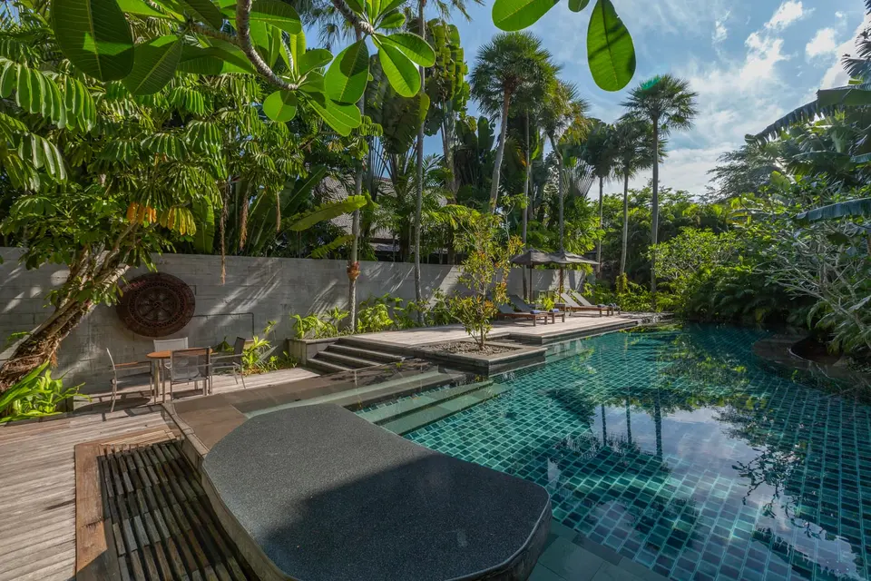 Pool omgivet af grønne planter med træterrasse, solsenge og siddepladser.