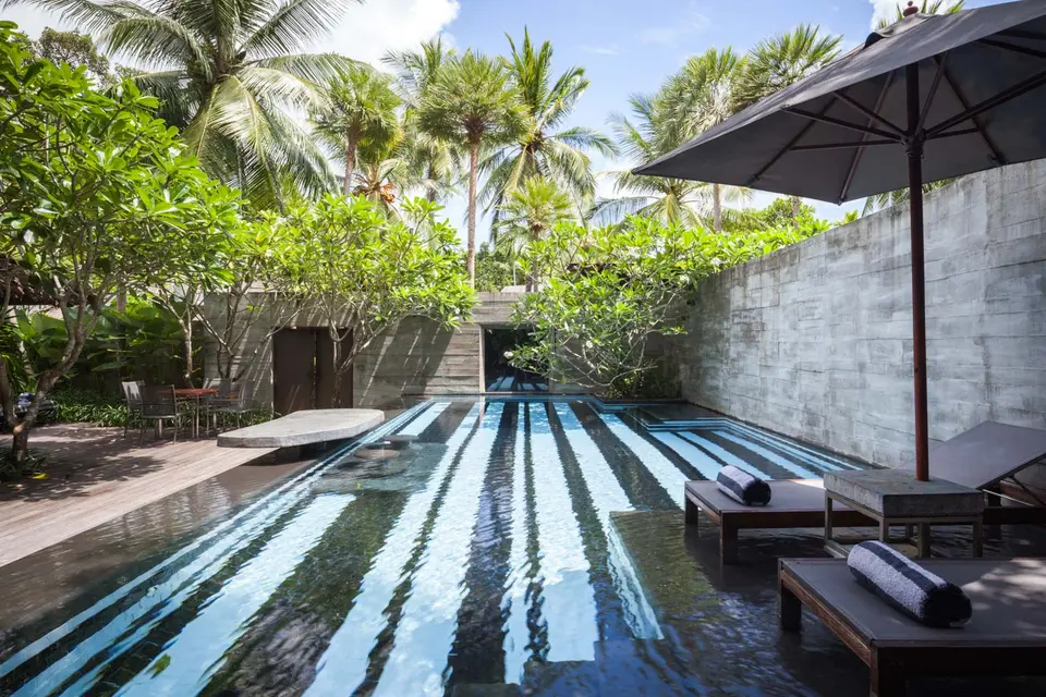 Elegant sort-hvidstribet pool omgivet af grønne træer og loungestole med håndklæder på eksklusivt resort i Sydeuropa.