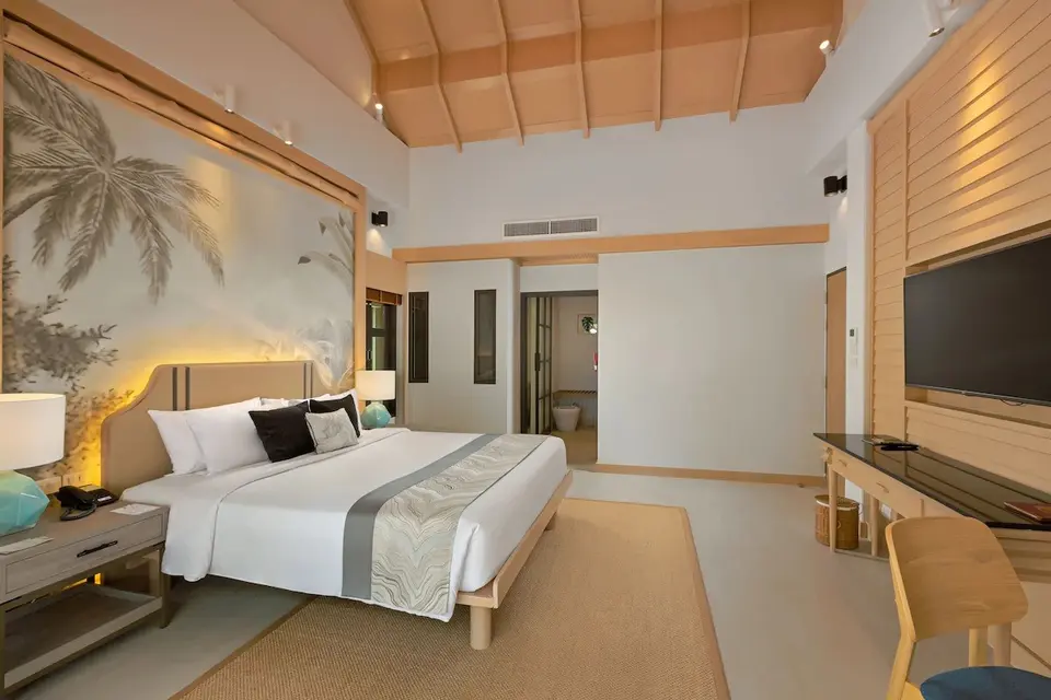 Lyst hotelværelse på Khaolak Merlin Resort med stor seng, palmetapet og åben adgang til moderne badeværelse.