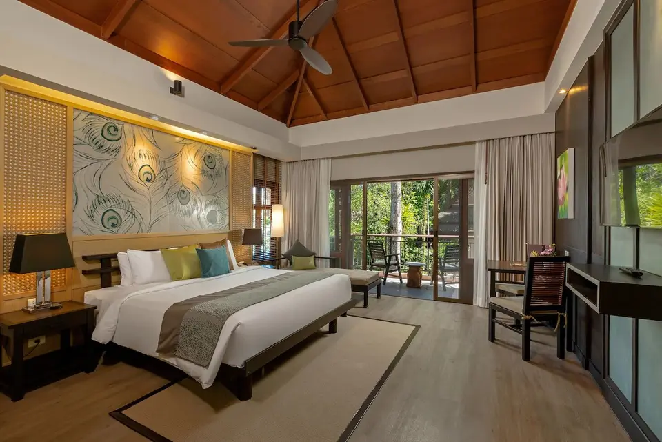 Lyst hotelværelse med stor seng og balkon med udsigt til grønne omgivelser på Khaolak Merlin Resort.
