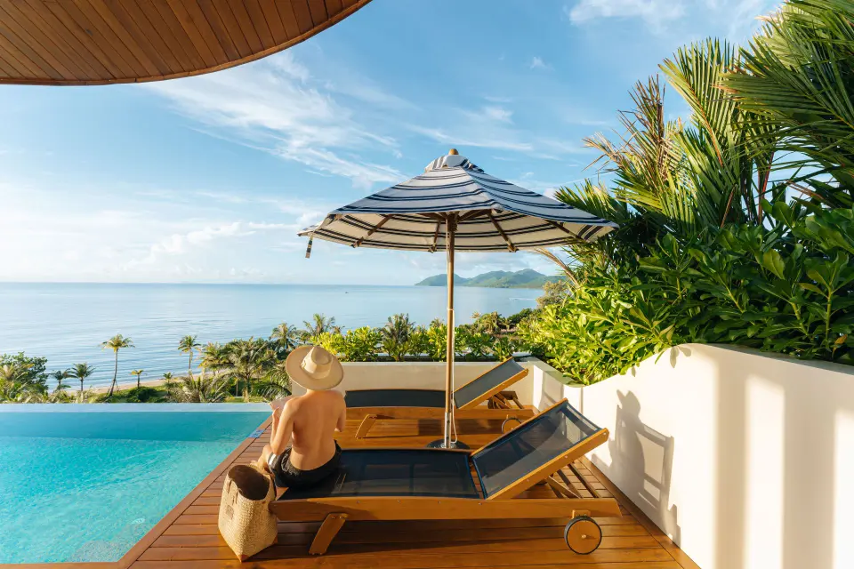 Gæst slapper af ved infinitypool med havudsigt og tropiske planter på Anantara Koh Yao Yai under stribet parasol.