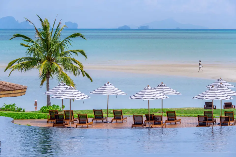 Træliggestole og stribede parasoller ved poolen på Anantara Koh Yao Yai med udsigt til strand, hav og grønne øer.