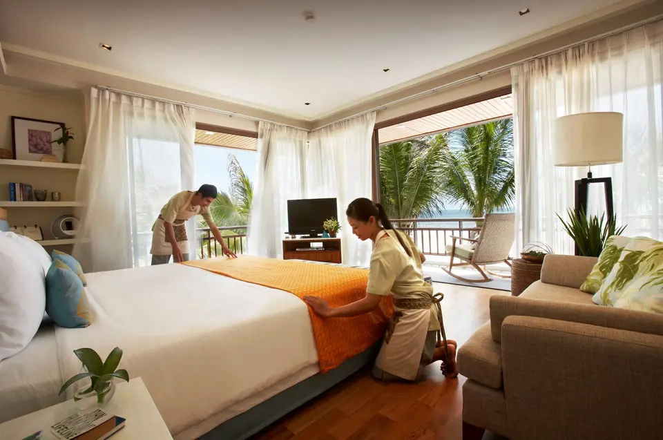 Hotelpersonale reder seng i lyst værelse med havudsigt og tropisk planter på Rest Detail Hotel Hua Hin.