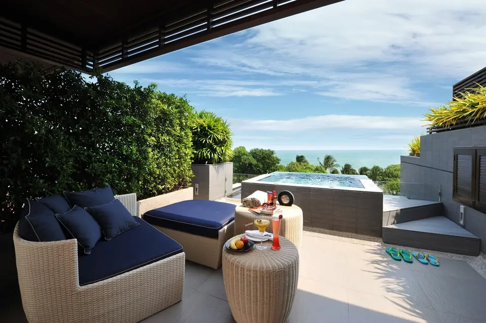 Terrasse med udendørs spabad, fletmøbler med blå hynder og udsigt mod havet.