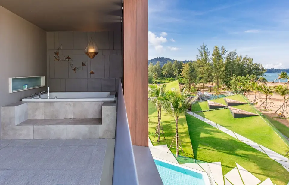 Lyst badeværelse med indbygget badekar åbner mod balkon med havudsigt på La Vela Khao Lak i Thailand.