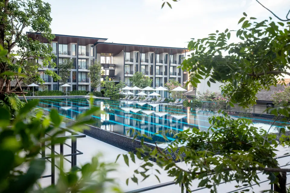 Modernistisk Varana Hotel i Krabi med store altaner og udsigt til frodig pool omgivet af grønne træer og hvide parasoller.