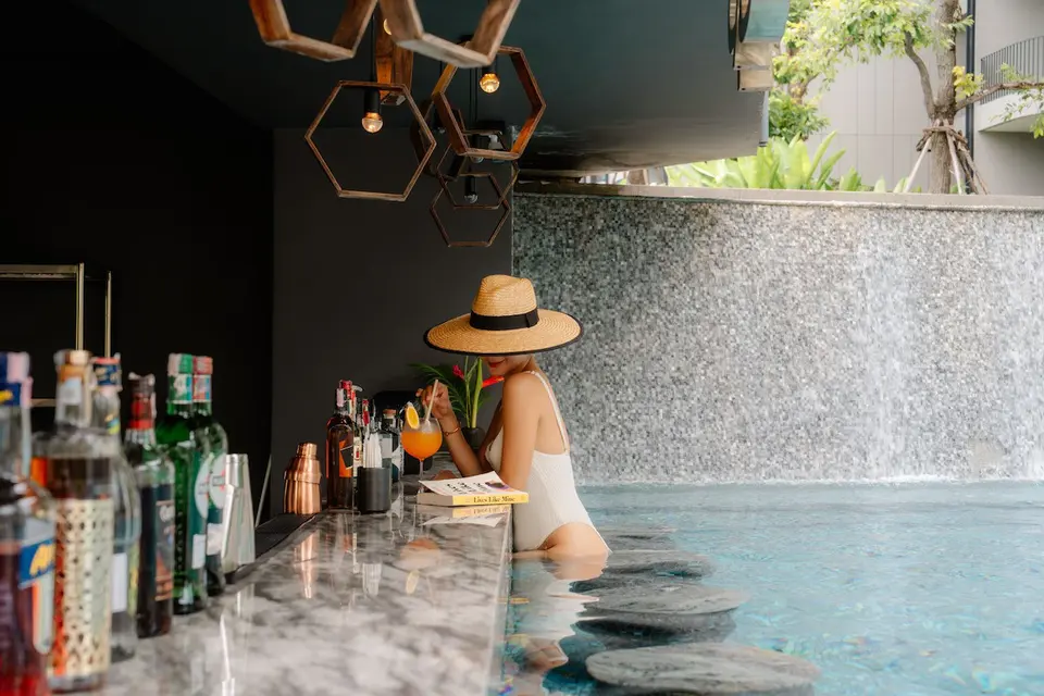 Gæst i hvid badedragt slapper af ved swim-up baren på Varana Hotel Krabi med drink og vandfald i baggrunden.
