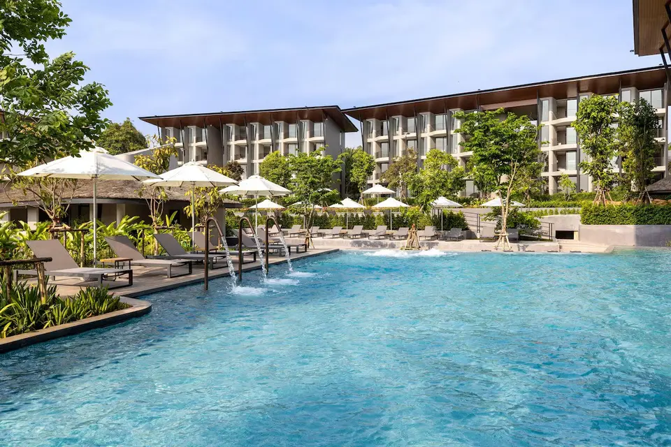 Udendørs poolområde med lounge-stole og parasoller omgivet af grønne planter foran Varana Hotel Krabi under blå himmel.