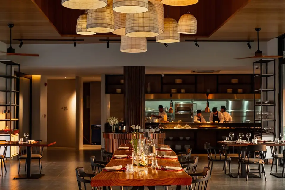 Restaurant med dækkede træborde, hængelamper og kokke i det åbne køkken.