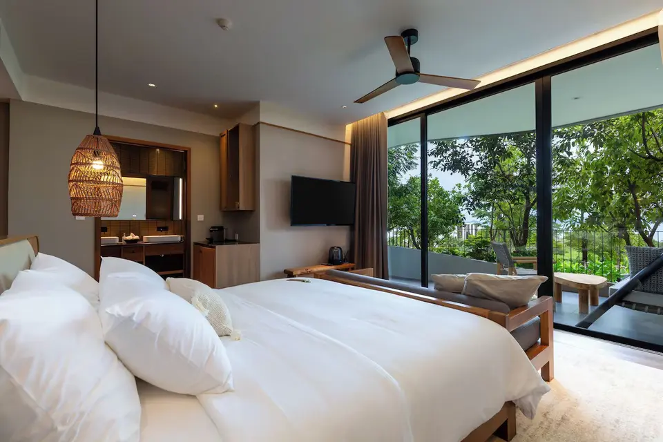Lyst hotelværelse på Varana Hotel Krabi med stor seng, balkon og rolig udsigt til grønne træer.
