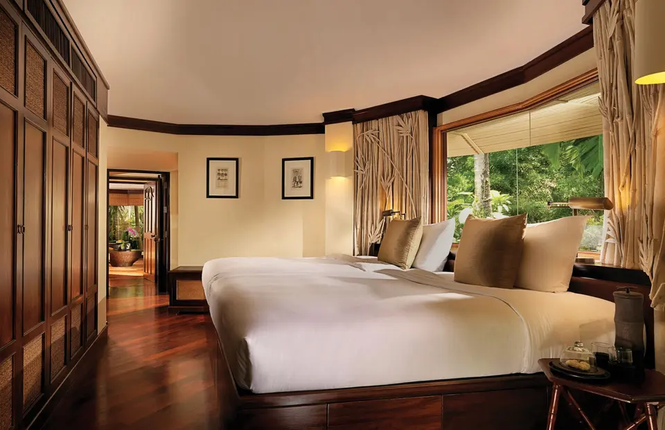 Elegant hotelværelse på Rayavadee Krabi med stor seng, trægulv og udsigt til frodig thailandsk jungle gennem vinduet.