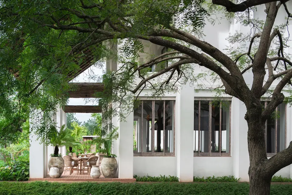 Modernistisk villa med store vinduer og overdækket terrasse omkranset af træer ved fredfyldt flod i Italien.