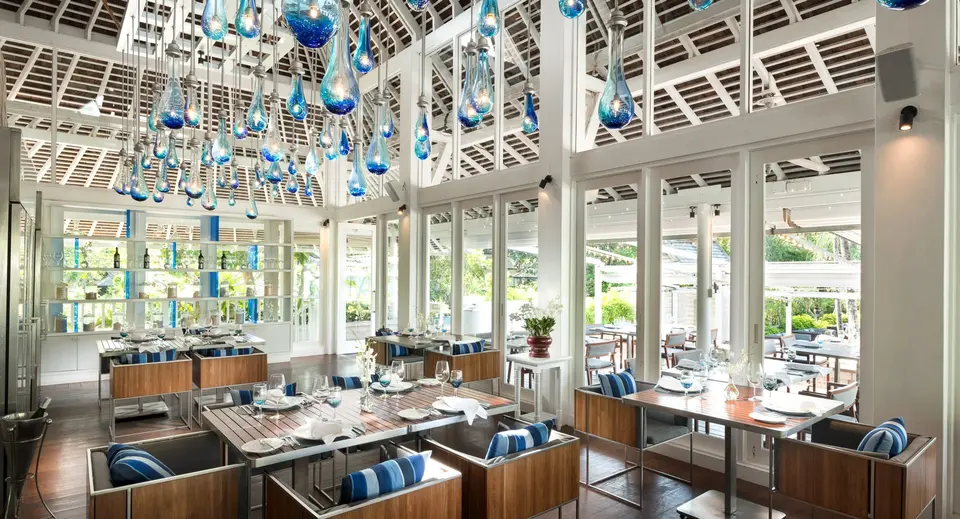 Lys restaurant med blå glaslamper, træborde og blåstribede puder.