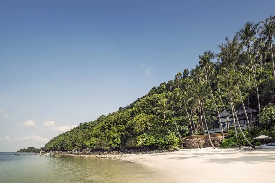 Luksusresort med stråtag gemt blandt palmer ved hvid sandstrand og krystalklart vand på Bali.