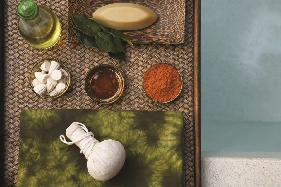 Urtekompres, olieflaske og små skåle med spa-produkter på en flettet bakke.