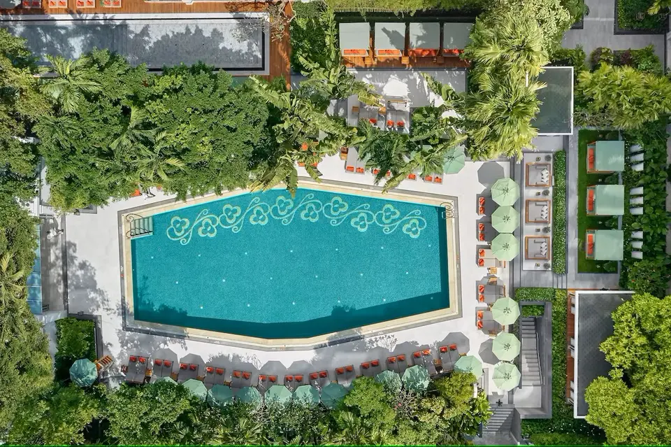 Rektangulær udendørs pool omgivet af grønne træer og solsenge på luksushotellet Mandarin Oriental i Bangkok.