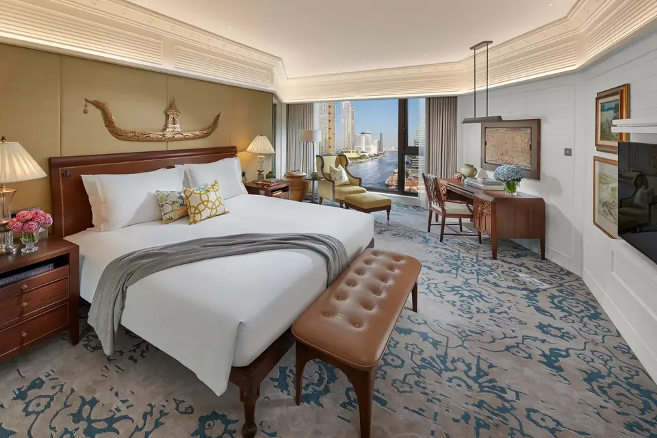 Elegant hotelsuite på Mandarin Oriental Bangkok med stor seng, skrivebord og panoramaudsigt over byens skyline.