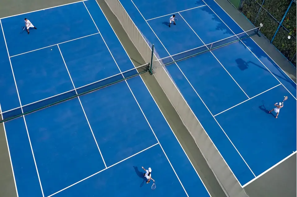 To blå tennisbaner med spillere set fra oven.