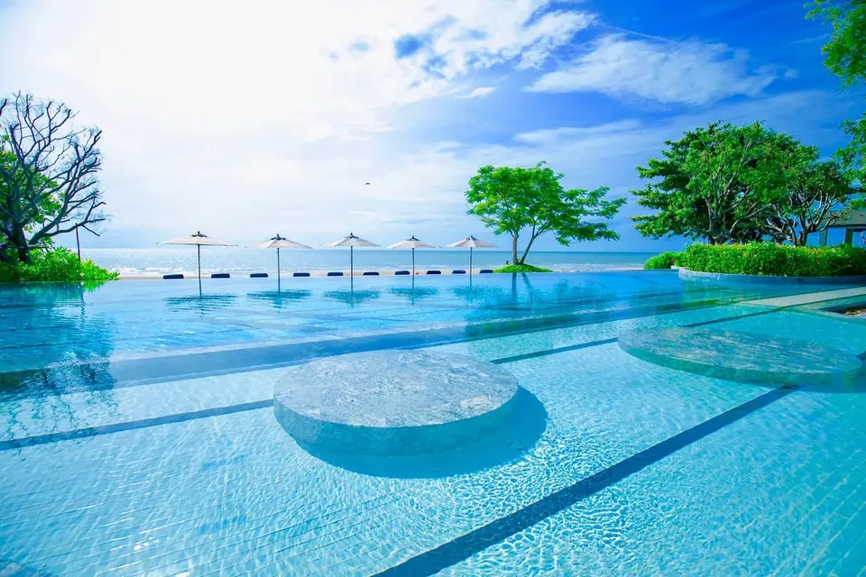 Infinity-pool med cirkulær siddeplads og havudsigt på Baba Beach Club, Hua Hin, omgivet af solsenge under blå himmel.